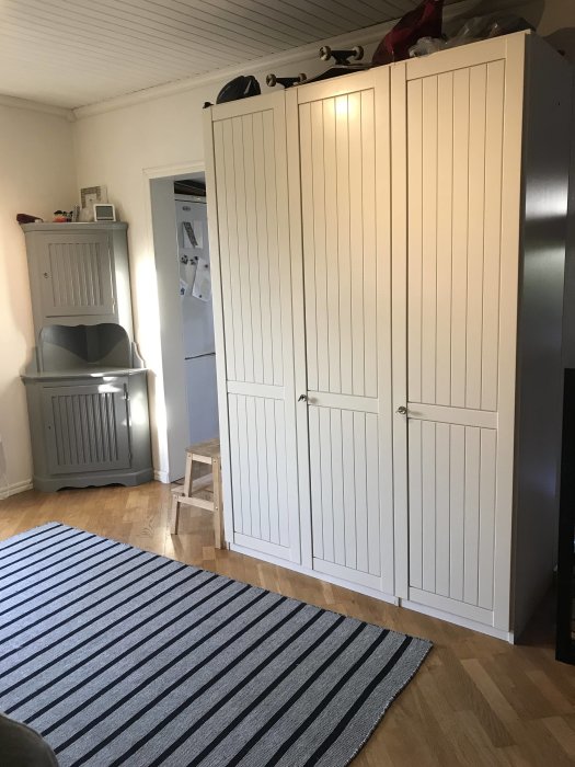 En hall med en vit garderob och ett vitmålat hörnskåp, som används för förvaring, intill en randig matta.