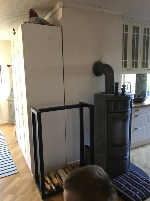 Ett vardagsrum med en fristående garderob vid väggen och en kakelugn; plats för tänkt hallförvaring och skafferi.