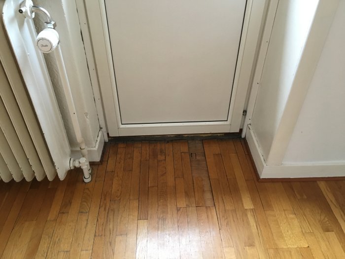 Skadad parkett framför balkongdörr där bitar av golvet har lossnat.