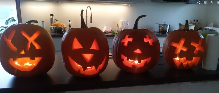 Fyra upplysta halloweenpumpor på köksbänk med olika utskurna ansikten.