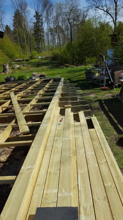 Ojämnt byggt träträdäck under konstruktion med synliga oregelbundna avstånd mellan reglarna och ofullständiga trallbrädor.