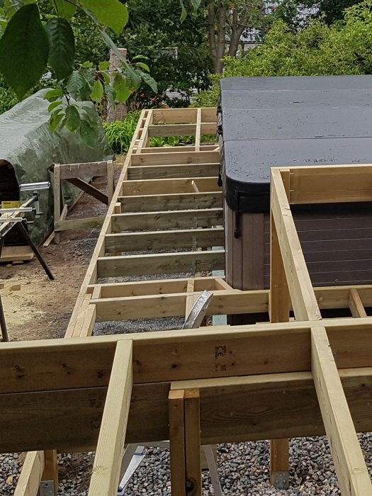 Uppbyggnad av poolområdets trästomme och plintar, med synliga stödben på betongplattor och nedgrävda plintar vid poolkant.