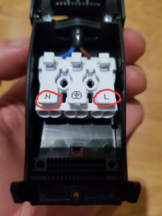 Eluttagets insida med två rödmarkerade knappar märkta "N" och "L" för trådanslutningar.