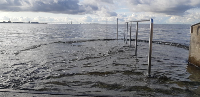 En badstege som leder ner i vattnet i Västra Hamnen med en bro i bakgrunden.