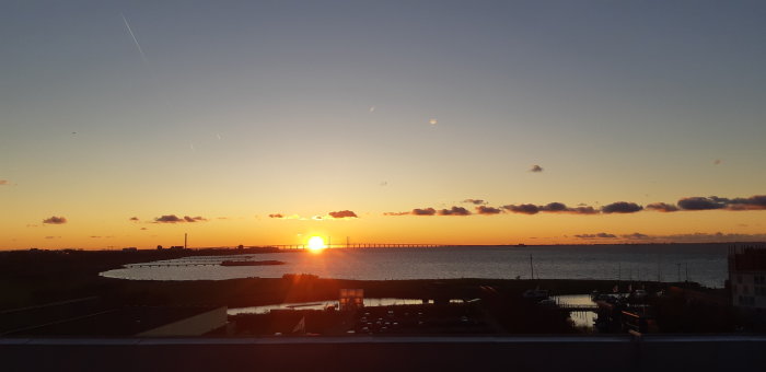 Solnedgång över Västra Hamnen med silhuetter av byggnader och bro mot en klar himmel.