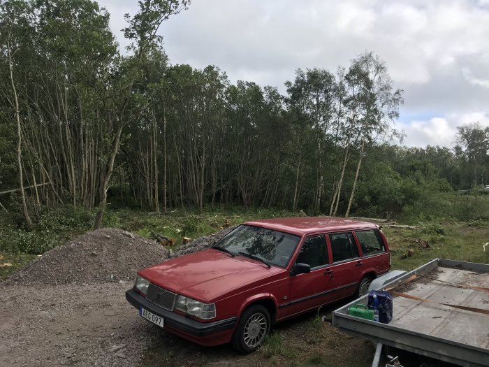 Röd kombibil parkerad vid nyfälld skog och högar av grus och grenar.