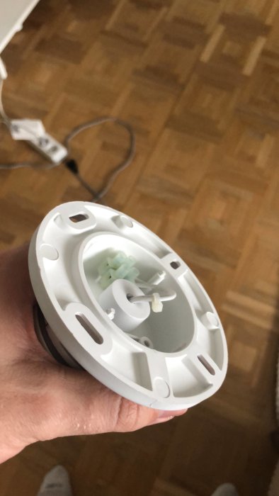 Taklampa hölje sedd uppifrån i handen över parkettgolv med kablar och plastklämmor.
