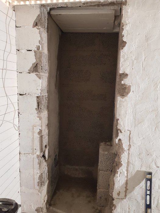 En ojämnt murad öppning i en vägg under renovering, med synliga lecablock och ett vattenpass som visar att murningen inte är helt lodrät.