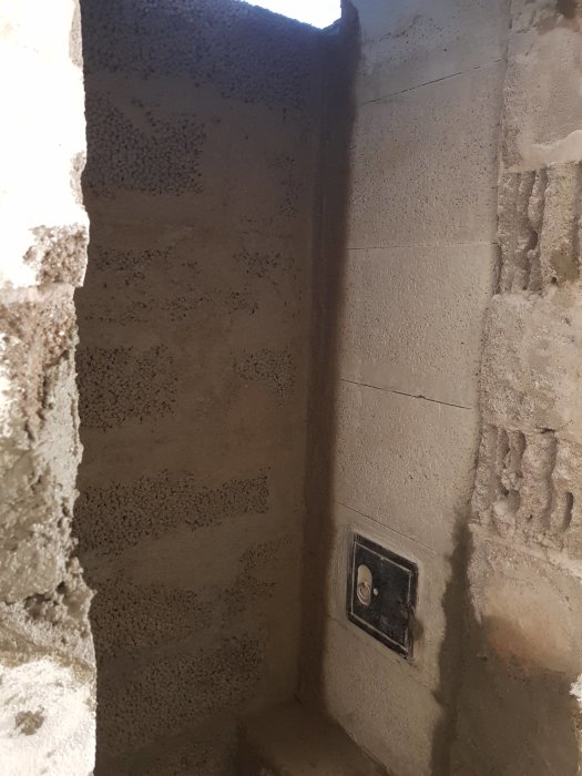 En bild av en murad öppning i källaren med synlig armering och en eluttagsdosa i förgrunden.