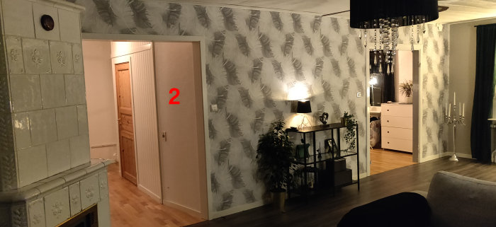 Inredning med vägg tapetserad med fjädermönster, öppen dörr vid nummer 2, kakelugn till vänster.