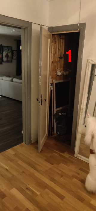 Interiör med öppen dörr till en skrubb under en trappa och synliga bjälkar.