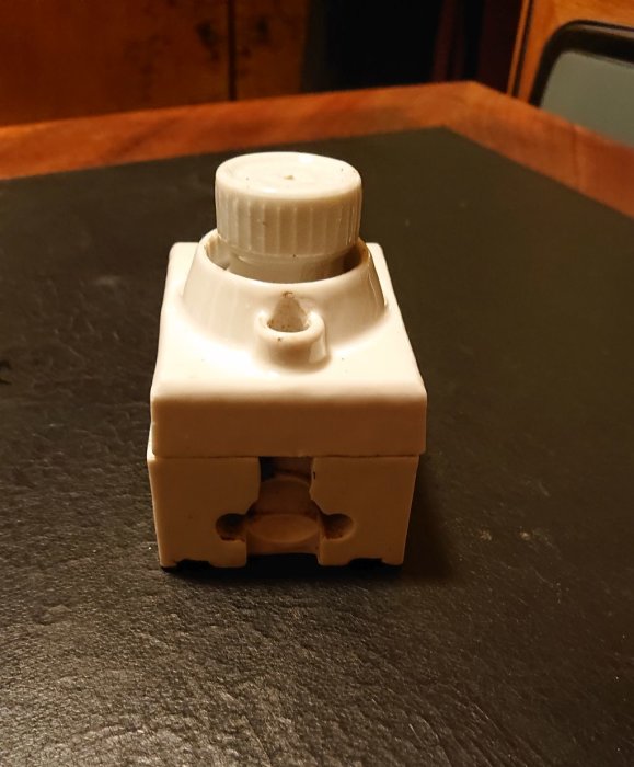 Gammal säkring med vit gängad propp i en keramisk hållare på bord.