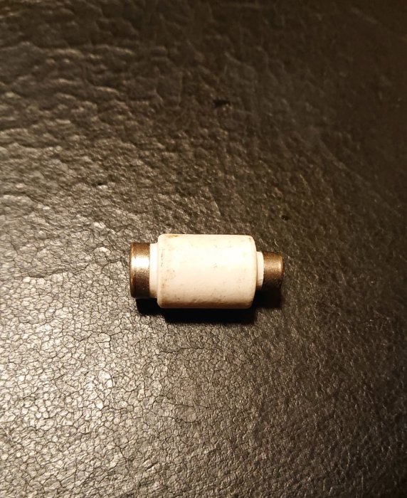 Gammal säkring med gänga och pappershölje, märkt 10A - 1,5mm², ligger på en svart yta.