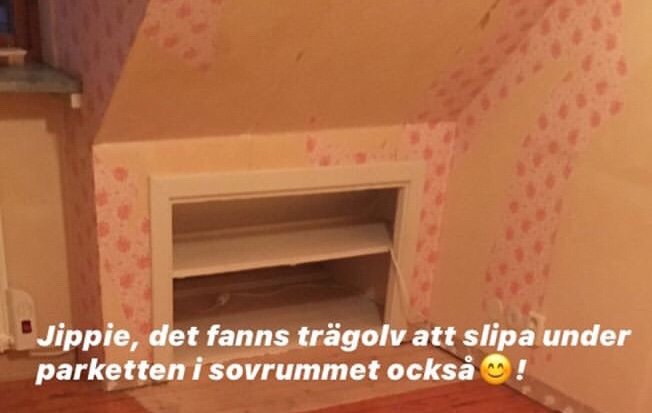 Ett öppet fack i väggen av ett sovrum med trägolv och tapetserade väggar, nedsänkt för klädförvaring.