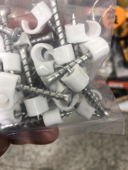 Plastkabelklämmor med skruvar i en genomskinlig påse, avsedda för montering av kablar.