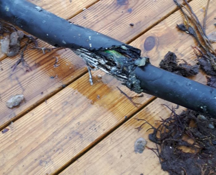 Skadad undervattenskabel med exponerade trådar och isolering på ett trägolv, tecken på elektriskt fel.