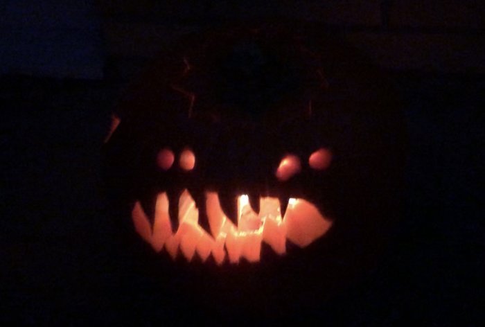 Upplyst halloweenpumpa med skuret ansikte i mörker.
