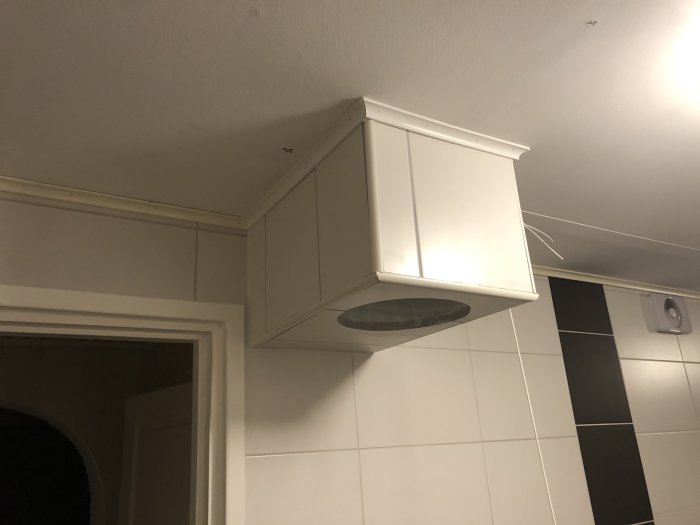 Vitt kaklat tvättnedkast med ojämna vinklar mot kaklade väggar, inbyggt i ett ojämnt snickrat skåp.
