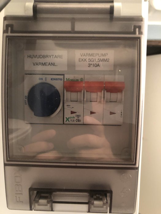 Säkringsskåp med huvudbrytare för värmepump och etiketter som anger specifikationer.