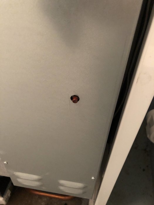 Grått plåtskydd med ett litet hål där man kan se något rött innanför.
