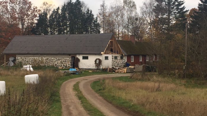 Landsbygdsstuga under renovering med en ny tillbyggnad i trä som kontrasterar mot den äldre stenbyggnaden.