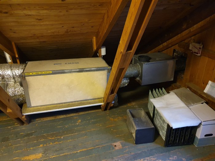 FTX-aggregat och filterlåda på vinden nära trätak och lutande vägg, röranslutningar syns.