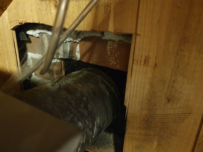En trång installation av ett ventilationsrör genom en utskärning i en trärörelse, som visar lite utrymme för att dra ett nytt rör.