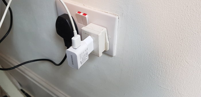 Eluttag med en adapter från brittisk till europeisk standard och en vit Samsung-laddare inkopplad.