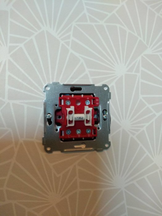 El-installation med öppen dosdimmer utan ram och knappar, synliga skruvar och anslutningar mot vägg med mönster.