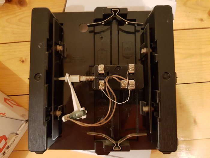 Ny ringklocka öppen baktill med två plintar för inkoppling, intill gröna och vita kablar.
