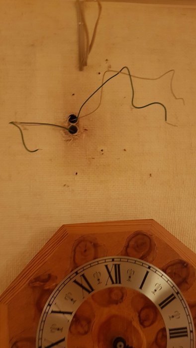 Vägg med utstickande gröna och vita kablar ovanför en del av en klocka.