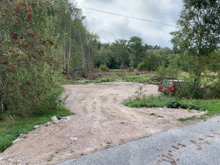 Nyutlagd grusplan som förstorad infart vid sommarprojekt med röd bil och grönska i bakgrunden.