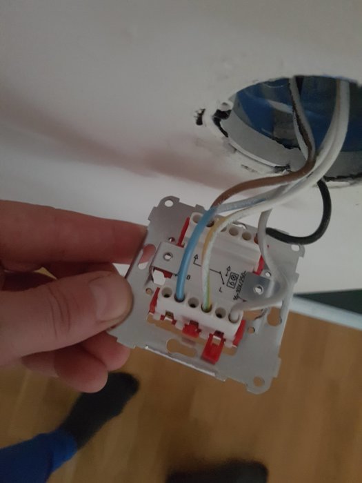 Hand håller en elbrytare med synliga ledningar och etiketter inför byte till dimmer.