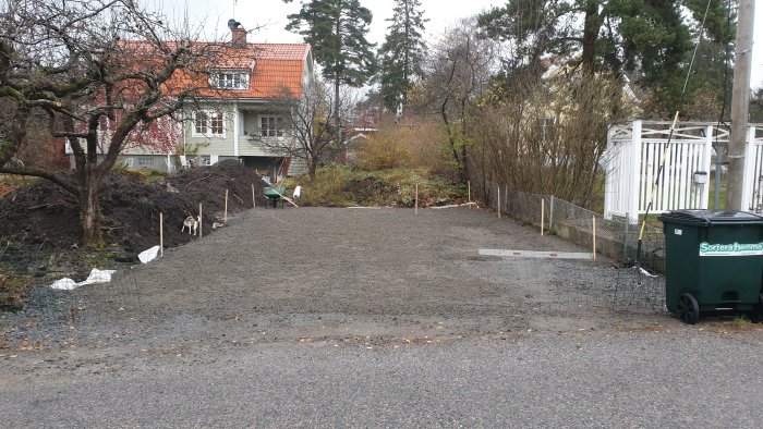 Nygrusad uppfart med stödmurar i process med hus och trädgård i bakgrunden.