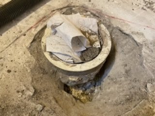 Gamla golvbrunnen utan slangar i ett betonggolv med synlig frigolitisolering.