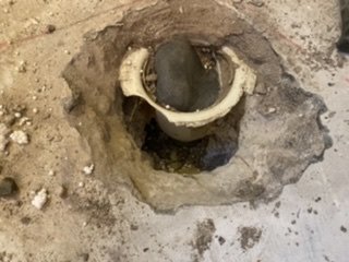 Borttagen golvbrunn med synlig anslutning och omgivande betong och frigolit i ett renoveringsprojekt.