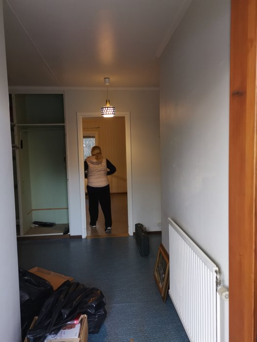 En hall före renovering med blå matta, en person i dörröppning och oordning på golvet.