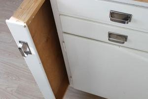 Vit kökslåda öppen, visar en utdragbar skärbräda i ek, bredvid en stängd låda med metallhandtag.