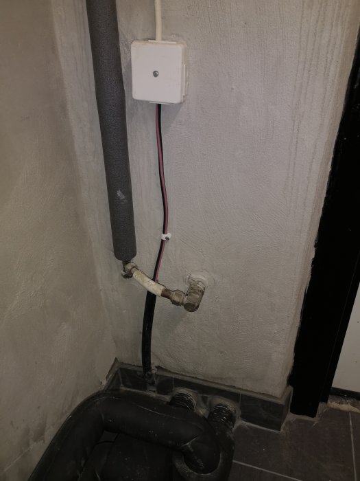 Elektrisk installation med en svart kabel som går in i väggen och en vit kabel som leder till en jordfelsbrytare.