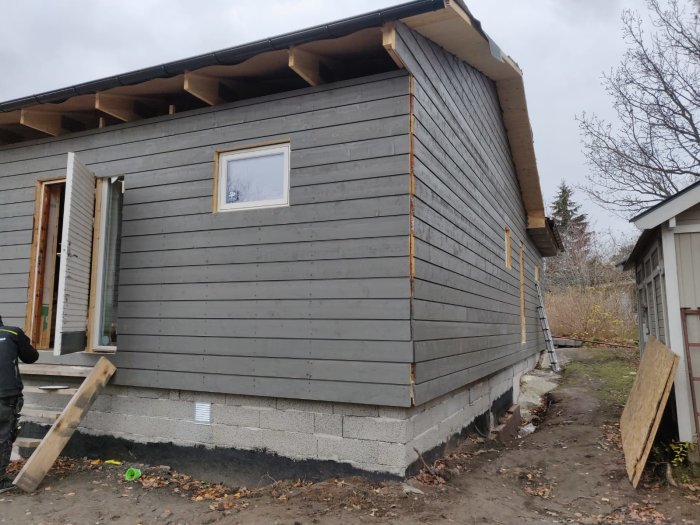 Hus under renovering med nyligen monterade fönster, dörrar och ny panel som är delvis målad.