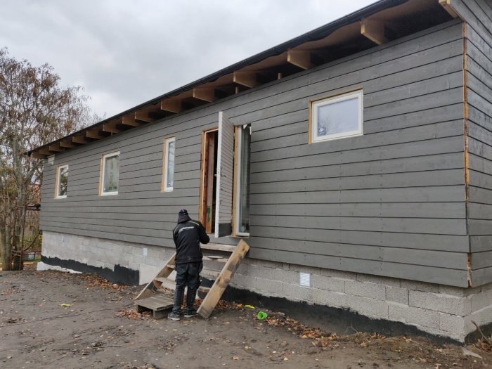 Hus under renovering med ny panel och fönster, och en person som arbetar på fasaden.