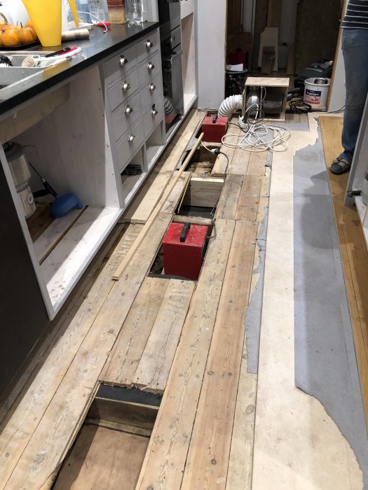 Kök under renovering med uppbrutet golv och synliga rör efter en vattenläcka.