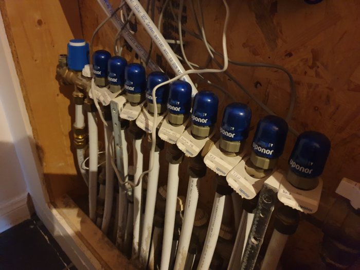 VVS-installation med flera vita rör och blåa ventiler märkta "Uponor" samlade vid en vägg.