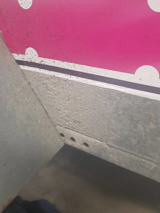 Närbild av ett släp med torkad grussprut på nedre delen och en rosa del med vita prickar ovanför.