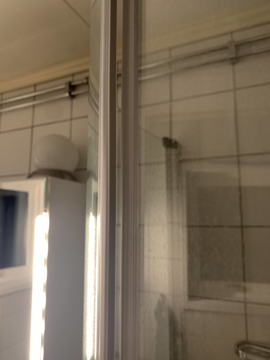 Nymonterad magnetlist på duschdörr, möjlig felmontering, med badrumskakel i bakgrunden.