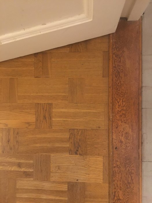 Trätröskel mot parkettgolv, möjlig teak, intill vit dörrpost.