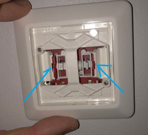 Hand som pekar på vita plastdelar inuti en eluttag ram där blå pilar markerar tryckpunkter.