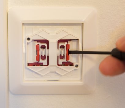 Hand demonterar eluttagets ram med skruvmejsel, visar snäppen.