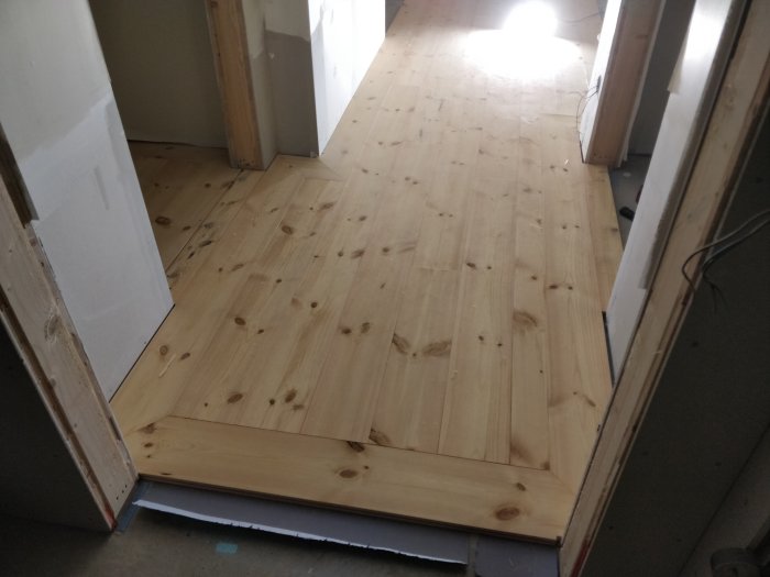 Nylagda massiva trägolv av furu i en hall med naturligt ljus från dörren.