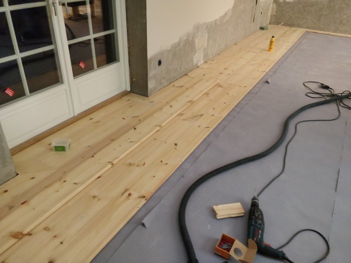 Installation av ett massivt trägolv av furu i ett rum med verktyg och byggmaterial synliga.